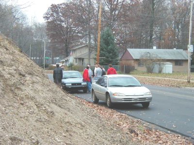 1997 Ford Taurus - Two cars are parked on a residential street with several people standing nearby.