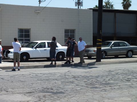 2003 Ford Crown Victoria - Several men talking on a sidewalk between a white Panther sedan and a gray luxury sedan outside a building