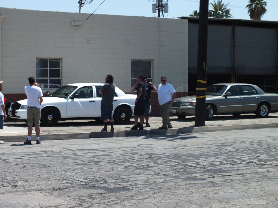 Group of men standing at a curb beside a white Crown Victoria and a gray Lincoln Town Car