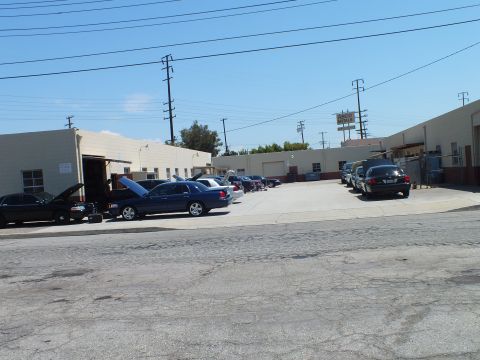 2003 Ford Crown Victoria - Wide view of a shop yard with several dark Panther sedans, two with hoods raised, utility poles overhead