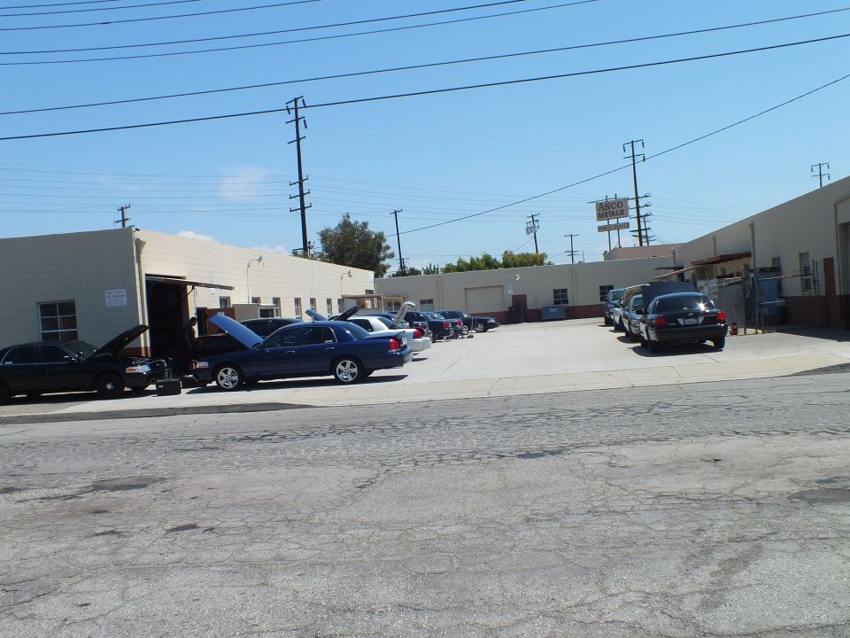 Industrial garage lot with dark sedans parked nose-in, hoods up, power lines and billboard behind