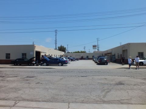 2003 Ford Crown Victoria - Street-level wide shot of a garage complex, dark sedans parked along the bays, two people standing at the right