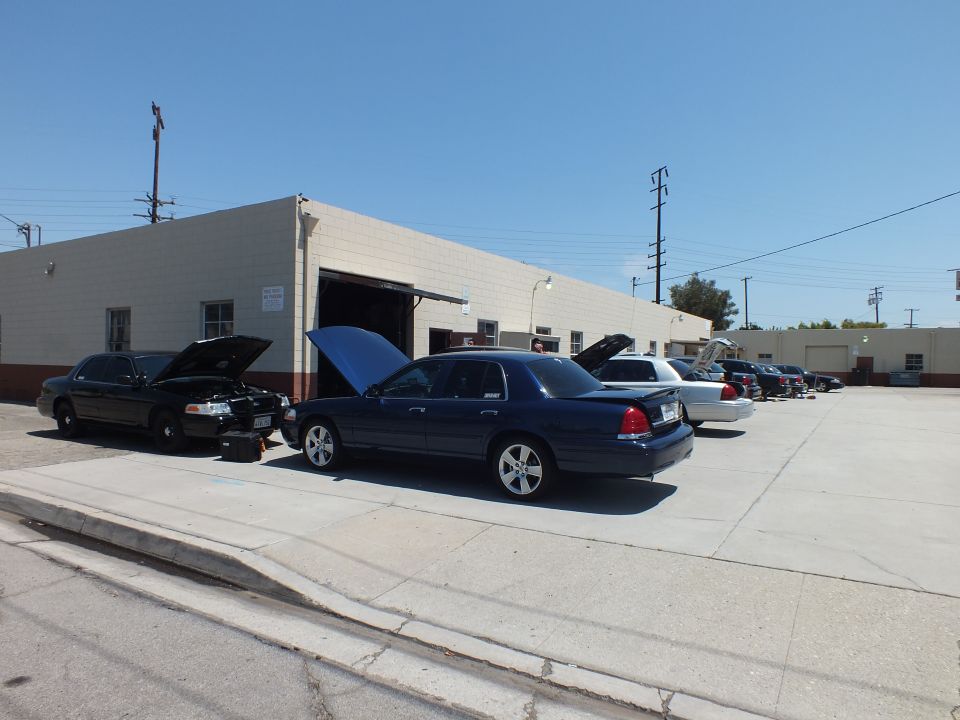 Black Crown Victoria and blue Mercury Grand Marquis with open hoods parked outside a garage bay