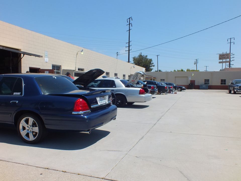 Blue Mercury Grand Marquis with spoiler and row of sedans parked along an industrial garage lot
