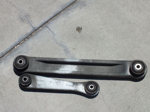 2003 Ford Crown Victoria - pair of stamped-steel suspension control arms with pressed bushings on a cracked concrete floor