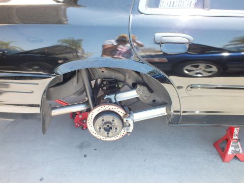 2003 Ford Crown Victoria - Black sedan rear corner stripped to the hub, exposing a drilled brake rotor and aluminum suspension arms