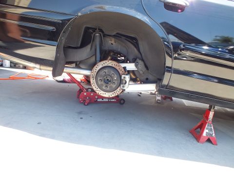 2003 Ford Crown Victoria - Rear corner of a black sedan on a low-profile floor jack, drilled rotor and polished links visible