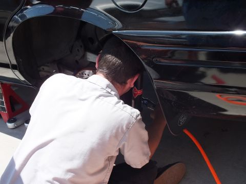 2003 Ford Crown Victoria - Close view of a worker reaching into a black sedan rear fender, Ford oval and orange air line visible