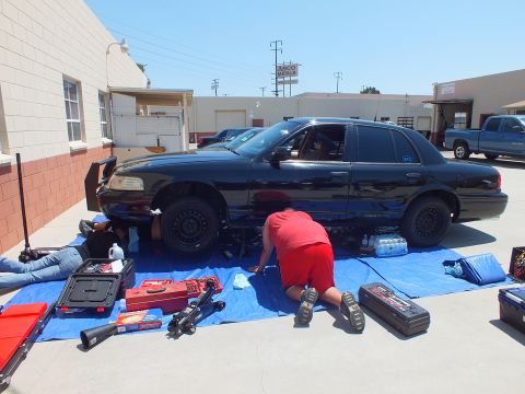 2003 Ford Crown Victoria - Black Crown Victoria lifted on a tarp, hood open and steel wheels off, tool chests laid out around it
