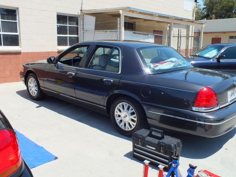2003 Ford Crown Victoria - Rear three-quarter of a dark blue Crown Victoria with chrome wheels parked by a building, red taillights