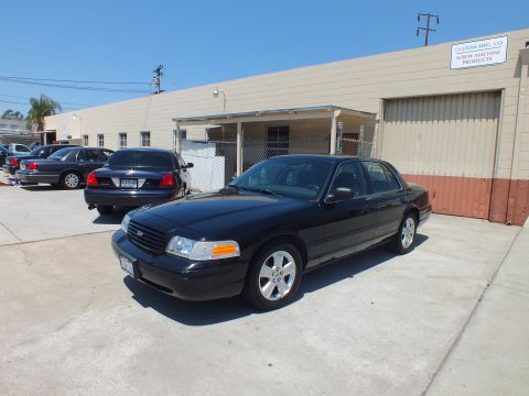 2003 Ford Crown Victoria - Black Crown Victoria with chrome wheels parked by a Custom Mfg warehouse, other sedans alongside