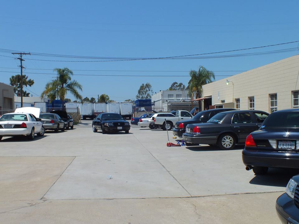 Industrial lot with white black and gray Ford sedans parked near palm trees and warehouses