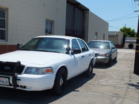 2003 Ford Crown Victoria - Front three-quarter of a white Crown Victoria with push bar, gray sedan behind, near Modern Welding shop