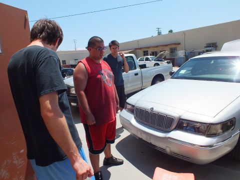 2003 Ford Crown Victoria - Three men stand looking at the chrome grille and headlight of a silver Mercury Grand Marquis outdoors.