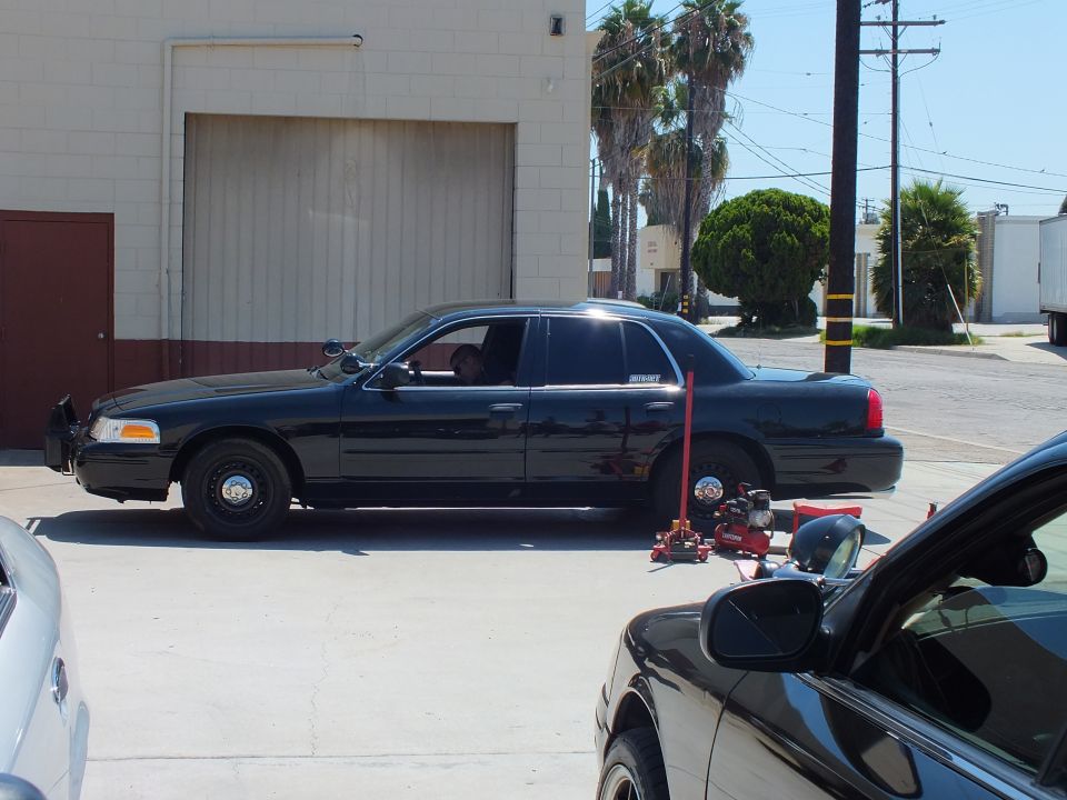 Black Ford Crown Victoria with front bumper removed parked at shop door