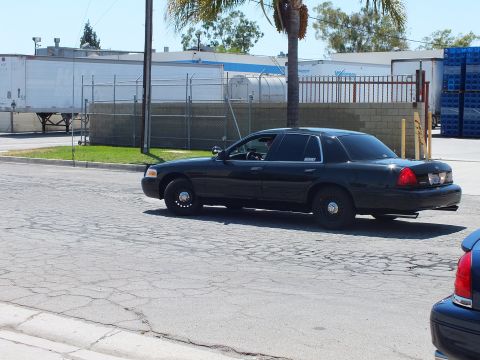 2003 Ford Crown Victoria - Blacked-out Ford Crown Victoria turning on a cracked asphalt street, fitted with plain dark steel wheels.