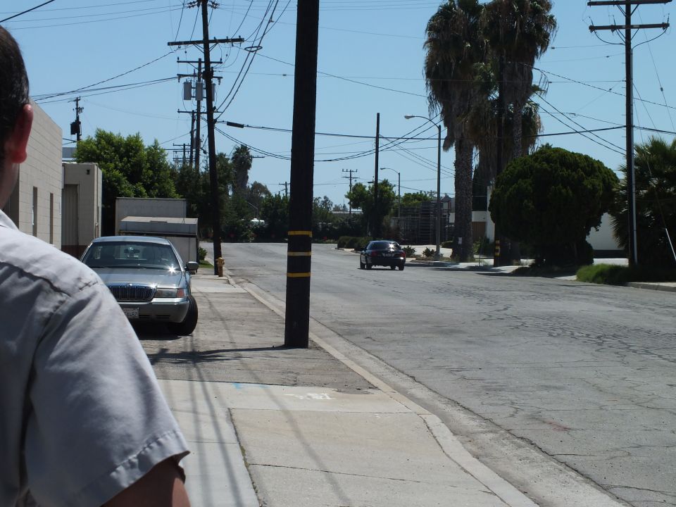 Man in gray shirt watches car drive down street past parked Mercury sedan