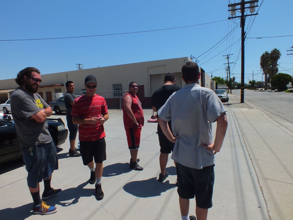 Group of men standing and talking in shop parking lot on sunny day