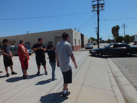 2003 Ford Crown Victoria - Men stand around an industrial lot near a black Ford Crown Victoria and a parked truck.