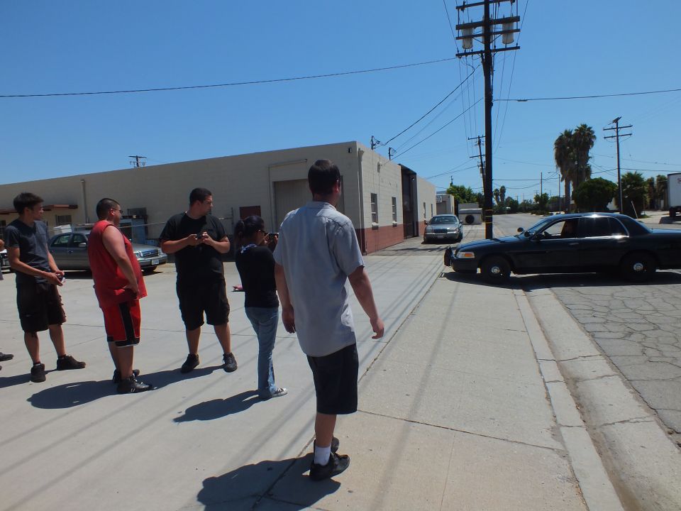 Group of men in shop lot beside black Ford Crown Victoria police-style sedan