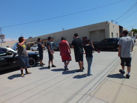 2003 Ford Crown Victoria - line of men walk across a concrete lot toward parked black sedans and an open shop bay.
