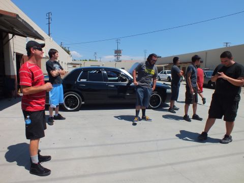 2003 Ford Crown Victoria - Several men stand around a lowered black Ford Crown Victoria with black wheels in an outdoor shop lot.