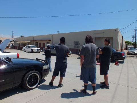 2003 Ford Crown Victoria - Men stand near a black Ford Crown Victoria with its hood up while a white Crown Victoria sits across the lot.