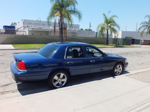 2003 Ford Crown Victoria - Side-rear view of a blue Mercury Grand Marquis parked by palm trees, riding on five-spoke chrome wheels.