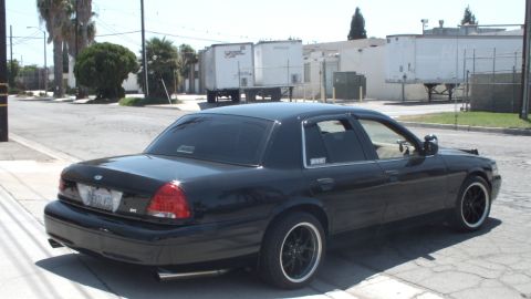 2003 Ford Crown Victoria - Black Ford Crown Victoria seen from the rear quarter, lowered on black wheels near an industrial street corner.