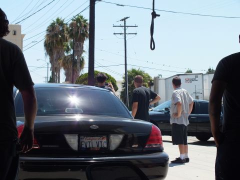 2003 Ford Crown Victoria - Black Crown Victoria SVT rear with California vanity plate EVTL VTC; men stand talking in the lot beyond.