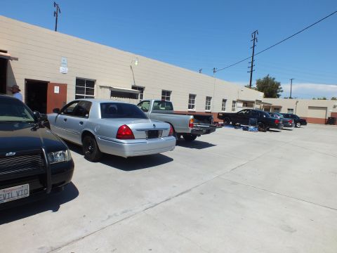 2003 Ford Crown Victoria - Silver Mercury, black Crown Victoria and a pickup parked in a row along a long industrial building.