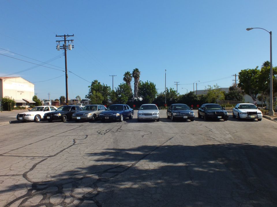 Eight Ford and Mercury sedans lined up facing camera across asphalt lot