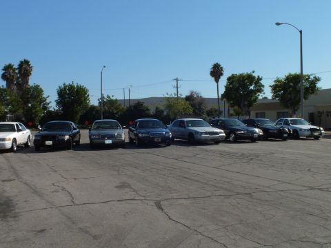 2003 Ford Crown Victoria - Dark and silver full-size sedans line up under a clear sky with low hills in the distance.