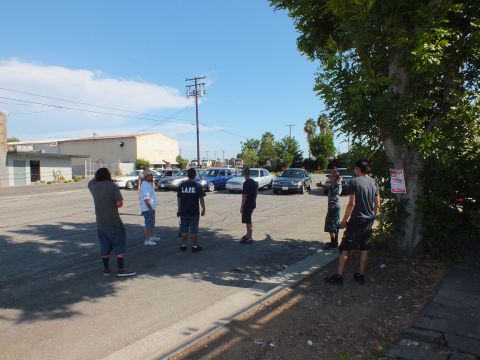 2003 Ford Crown Victoria - People gather curbside watching parked sedans; one wears a shirt reading L.A.P.D.