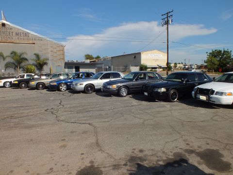 2003 Ford Crown Victoria - Full-size sedans angle across asphalt beside a building reading Custom Sheet Metal Engineering.