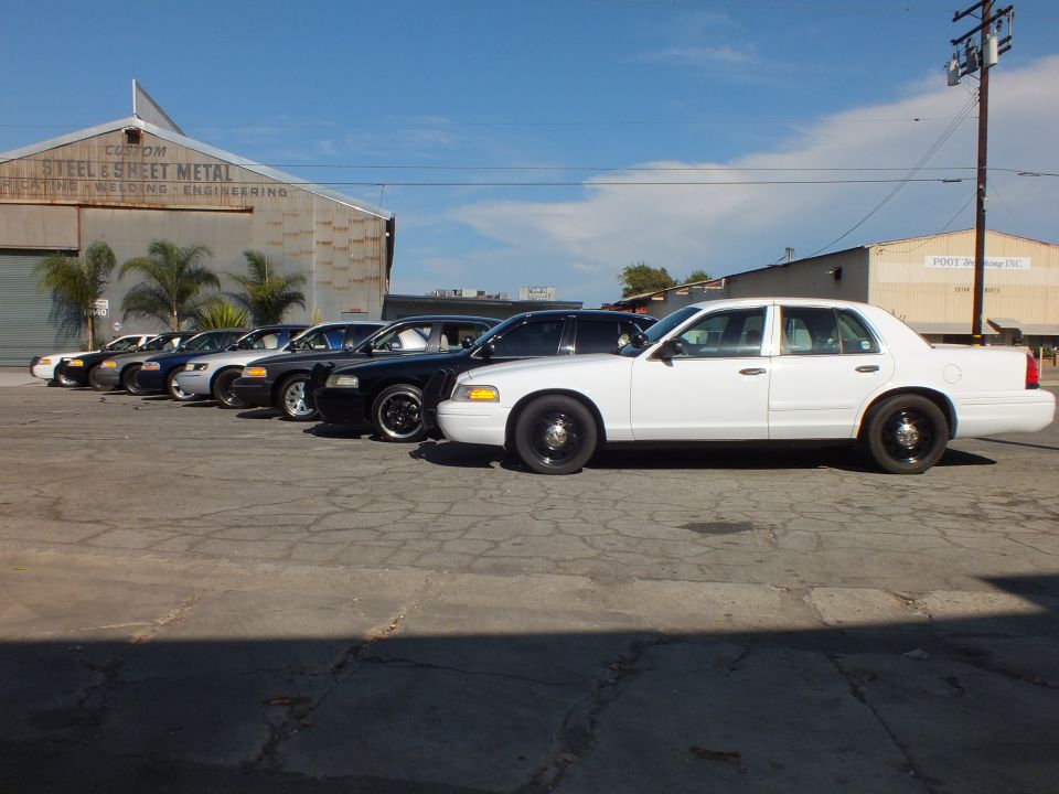 White Ford Crown Victoria at front of a sedan row beside an industrial warehouse