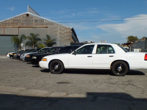 2003 Ford Crown Victoria - white Crown Victoria sits in profile ahead of a row of sedans by a Steel and Sheet Metal shop.