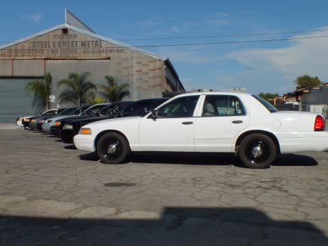2003 Ford Crown Victoria - white Crown Victoria on black steel wheels leads a sedan row beside an industrial building.