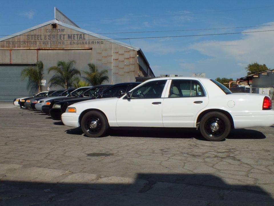 White Ford Crown Victoria in profile with black steel wheels by warehouse