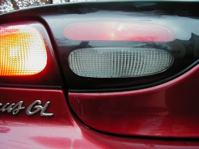 1997 Ford Taurus - Close-up of a red car's rear left tail light assembly, showing the 'GL' trim badge.