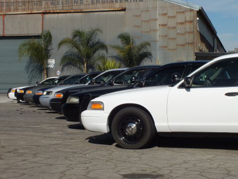 2003 Ford Crown Victoria - Front quarters of black-and-white Crown Victoria sedans line up tightly against a metal warehouse.
