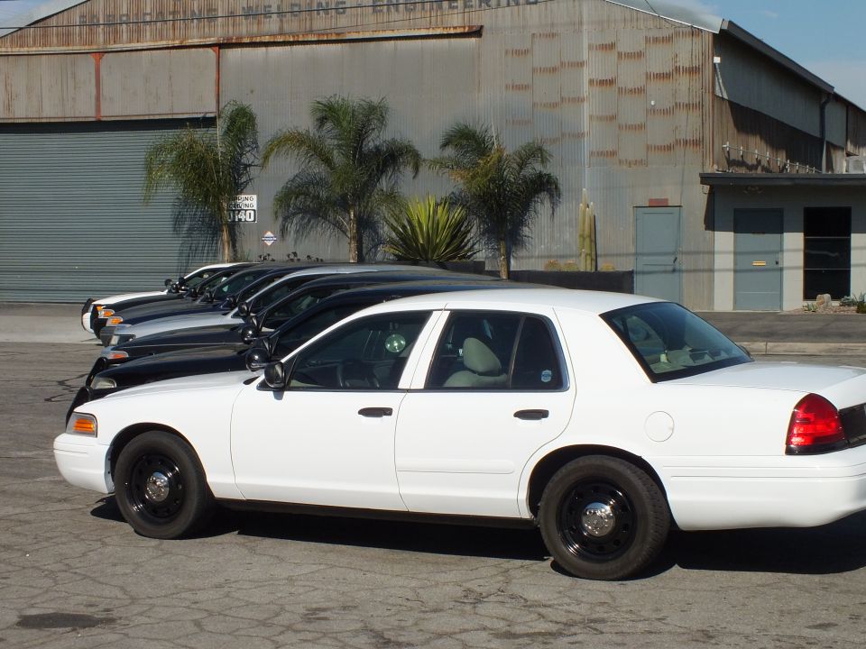 Side profile of white Ford Crown Victoria with black steel wheels in industrial lot