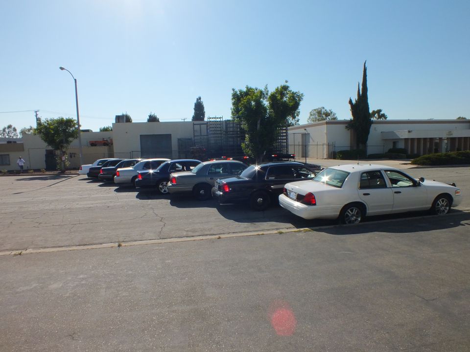 Row of full-size sedans parked diagonally in sunny industrial lot