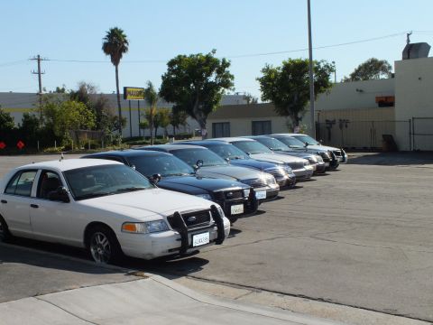 2003 Ford Crown Victoria - Front-quarter row of full-size sedans on asphalt near Maxon sign, white car with California plate nearest