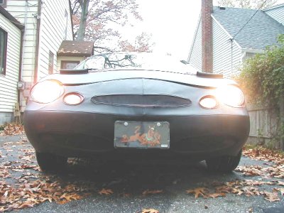 1997 Ford Taurus - Low head-on view of a dark sedan's front end with its headlights on, showing the rounded oval-themed nose, blacked-out grille area and a gr…