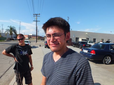 2003 Ford Crown Victoria - Man with glasses grimacing in foreground, second man with hand on hip, sedans and warehouse behind