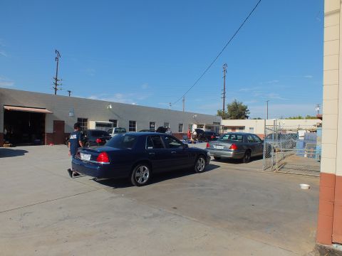 2003 Ford Crown Victoria - Lowered dark sedan in industrial yard with person in POLICE shirt, second car and garages behind