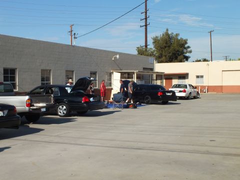 2003 Ford Crown Victoria - Group works on parked dark sedans with raised hoods, folding chairs and gear on the asphalt