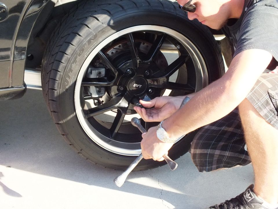 Person loosening lug nuts on black car with black SVT wheel and Nitto tire