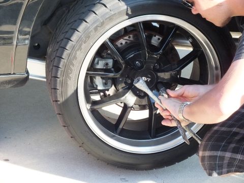2003 Ford Crown Victoria - wrench is pressed against the SVT-marked center cap of a black wheel mounted on a dark car